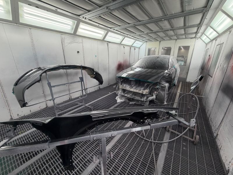 Hatchback in the spray booth with its front bumper and guard painted on stands