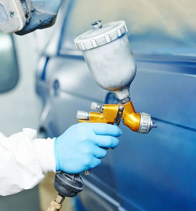 Technician spraying paint onto a blue car panel